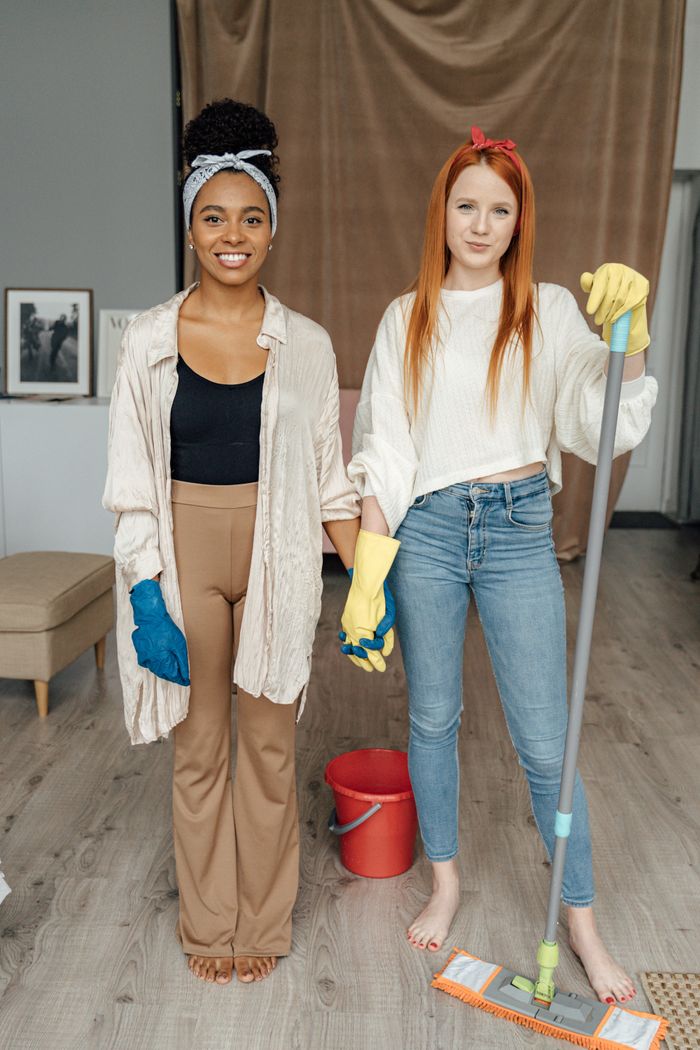 services-02 Two women smiling and holding hands while cleaning indoors, symbolizing teamwork.